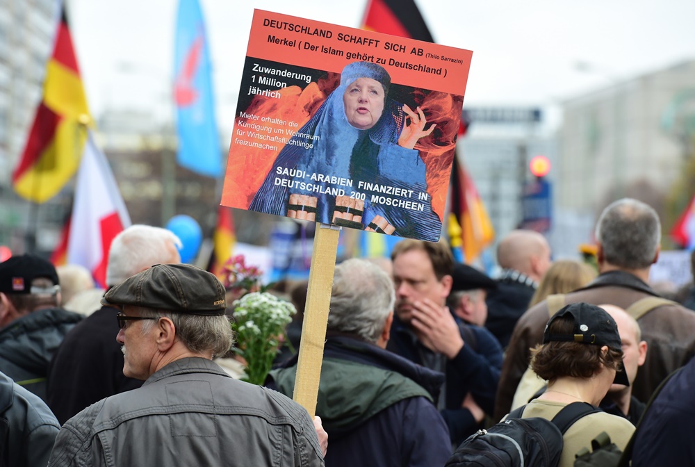 A supporter of the right-wing populist Alternative for Germany Party displays a placard showing Chancellor Merkel dressed in a Burqa during a demonstration against the German government’s asylum policy on November 7, 2015. AFP PHOTO /  JOHN MACDOUGALL