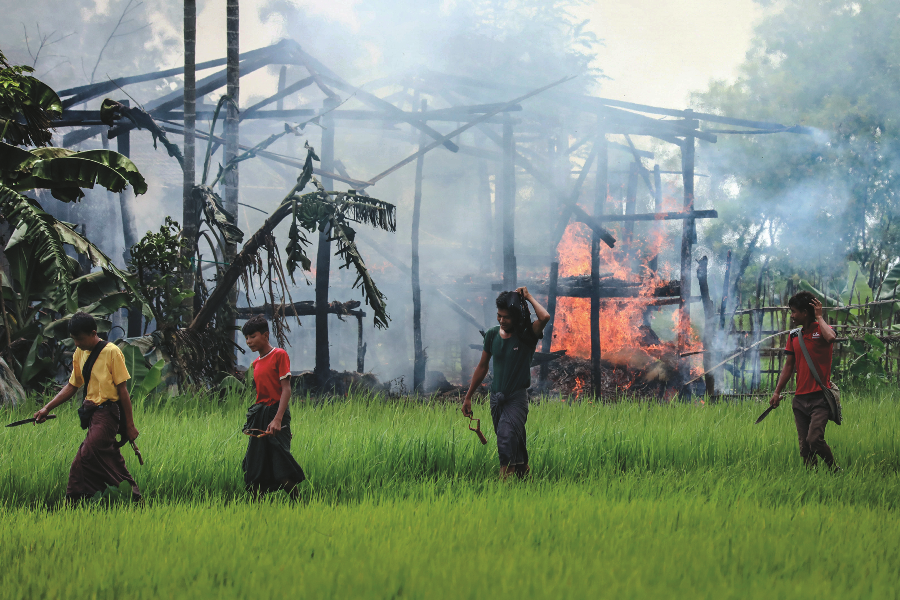 Rakhine mobs walk past a burning house in Gawdu Tharya village near Maungdaw in Rakhine State. Besides the violence of the military, the Rohingya were the target of the Rakhine mobs’ attacks as well.  AFP PHOTO / STR