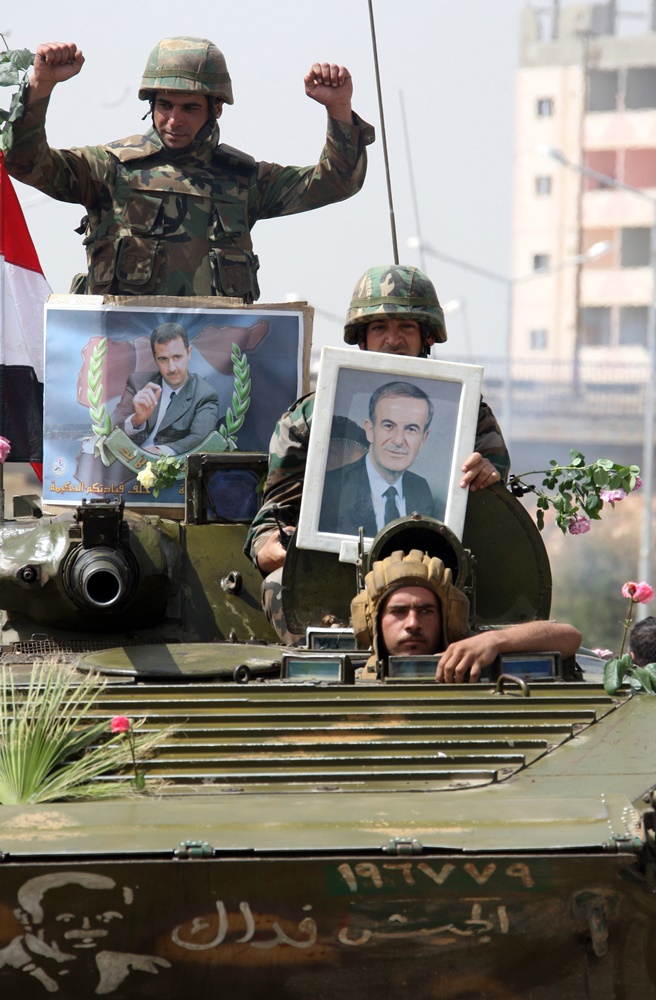Syrian army troops hold up portraits of President Bashar  al-Assad (L) and his late father, former president Hafez al-Assad, as they pull out of the southern protest hub of Daraa on May 5,  2011 after a military lockdown of more than a week during which dozens of people were killed in what activists termed as “indiscriminate” shelling of the town, some 100 kms south of the capital Damascus. AFP PHOTO / LOUAI BESHARA