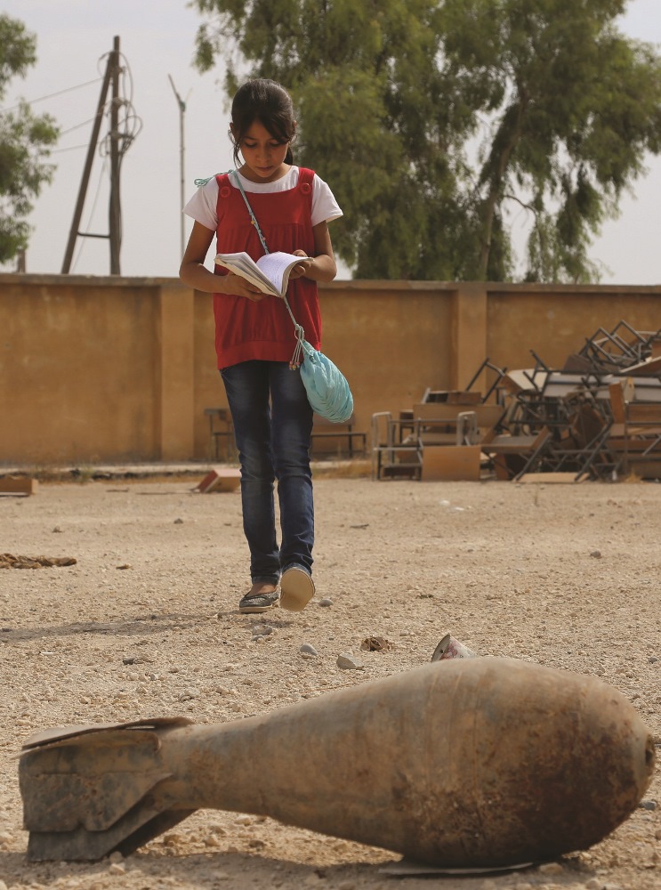 A Syrian youth walks near a mortar shell lying on the yard of her school on the second day of the new school year on October 6, 2015 in the Syrian Kurdish town of Kobane. | AFP PHOTO / DELIL SOULEIMAN